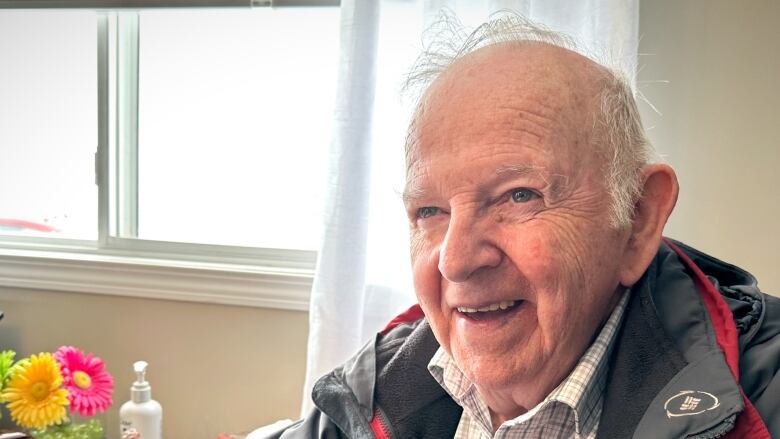 A man in front of a window smiles and talks to people off camera.