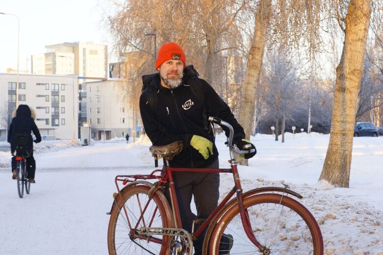 Man with frozen beard stands next to a bike in winter.