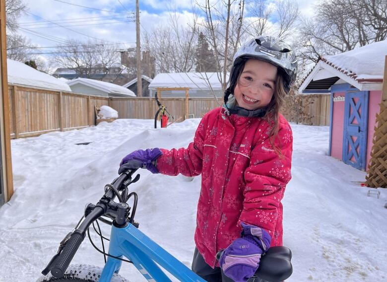 Young girl dressed in winter clothing smiles while leaning on her bike.