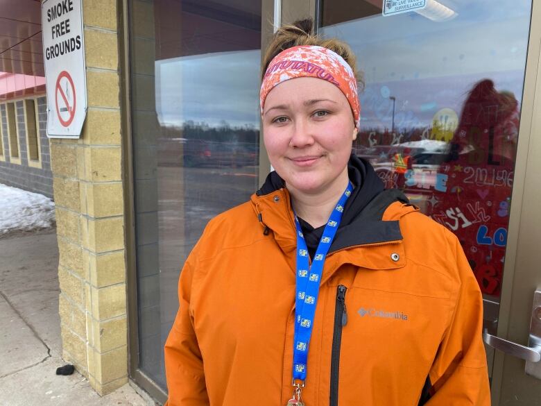 A smiling woman wearing an orange coat and bandana stands in front of a post office box.