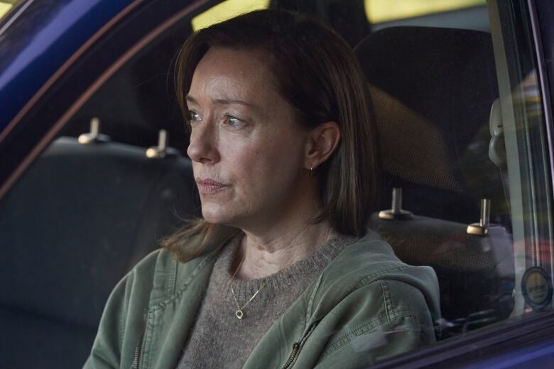 A woman sits in a car. She is staring away from the camera. 