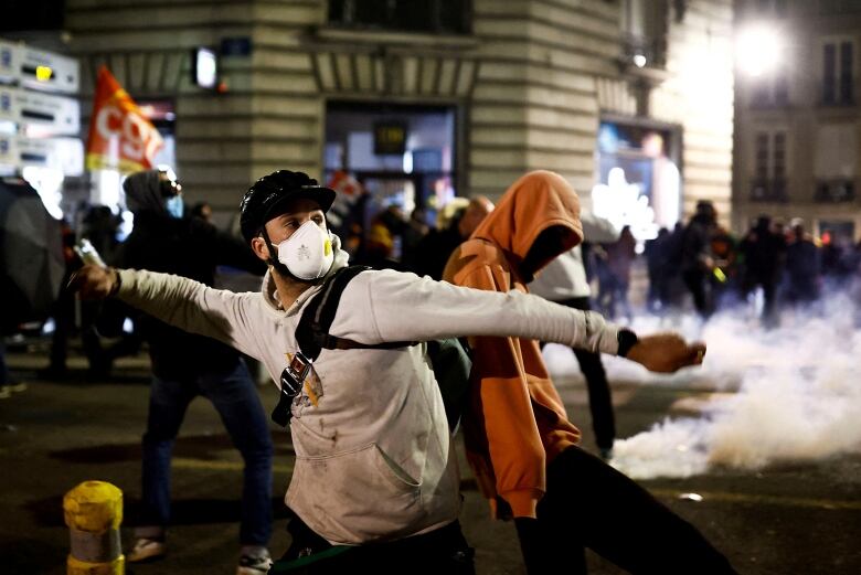 An individual in a white top and wearing a face mask and helmet holds his arm back as he prepares to throw something.