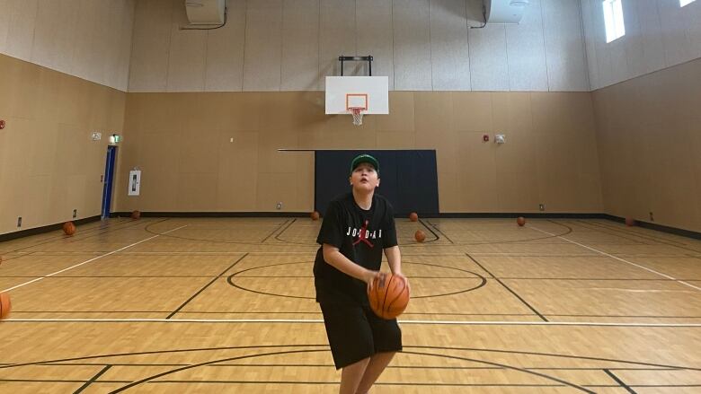 A kid holding a basketball looks up at the net 