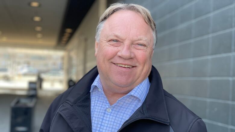 A man wearing a black jacket and blue checked shirt smiles