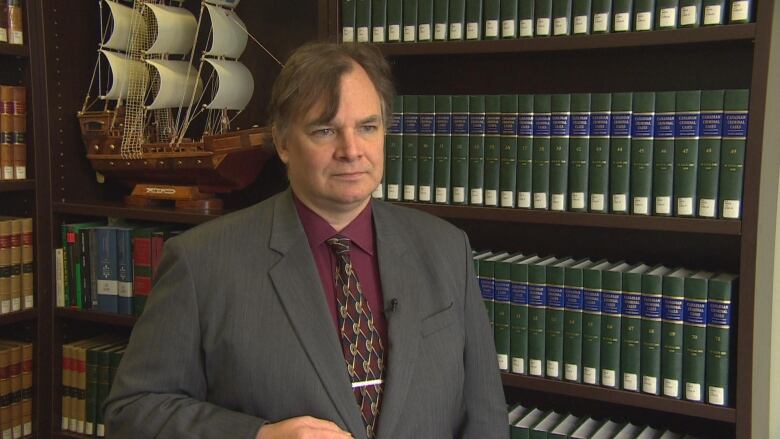 A man in a suit looks beyond the camera in front of bookcases.