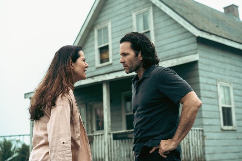 A woman and a man stand face-to-face in front of an old house.