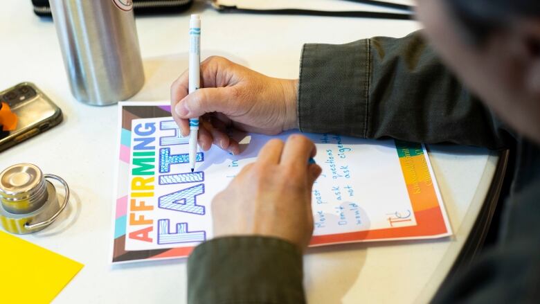 A person takes note on supporting the LGBTQ community on a piece of paper that has rainbows and says affirming ministry.