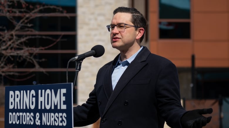 A man wearing a coat and gloves stands behind a podium.