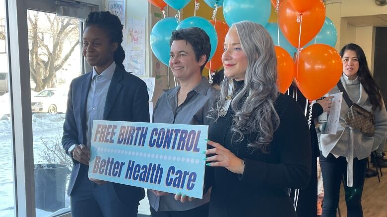 Three women stand up with a sign.