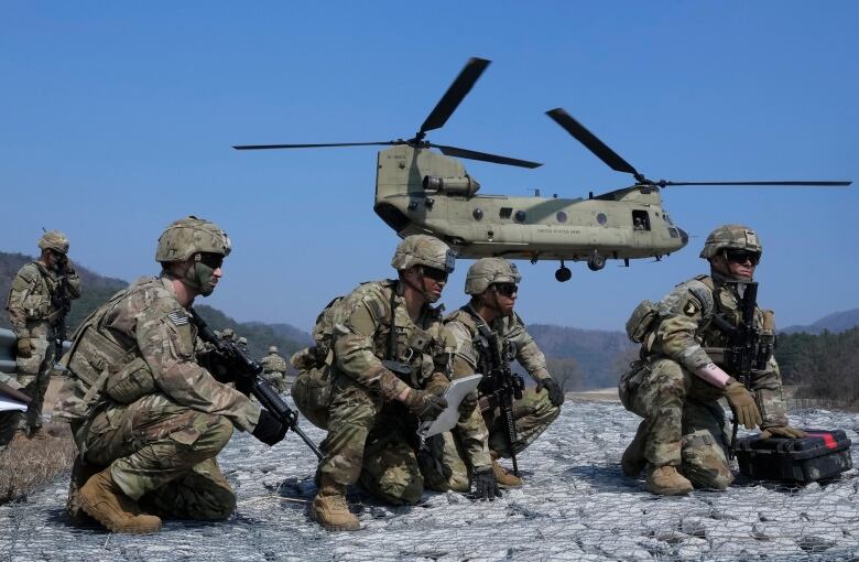 Soldiers crouch while a helicopters flies behind them during a military drill.