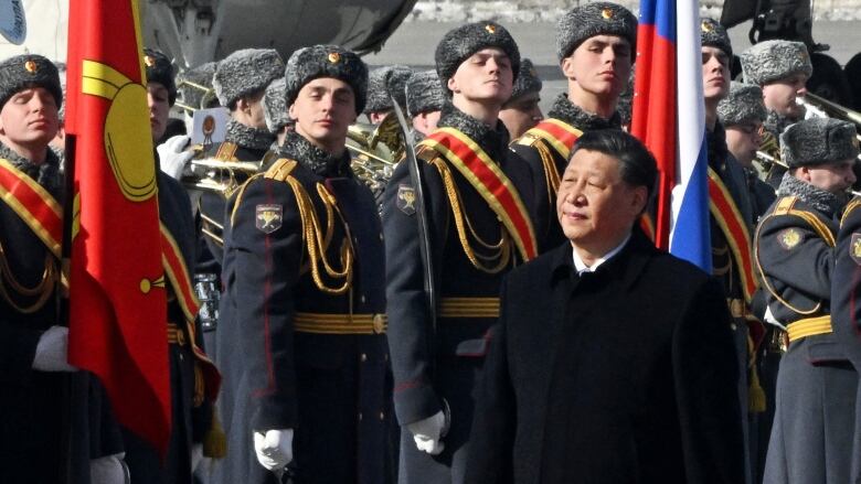 A man in a long coat is shown walking in front of guards. 