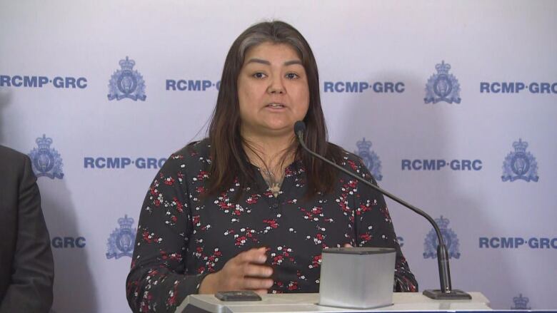 A woman with dark hear and a navy shirt with red and white patterns speaks into a microphone.