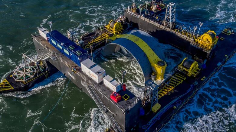 A large floating structure with a giant cylindrical tidal turbine in the middle of it.