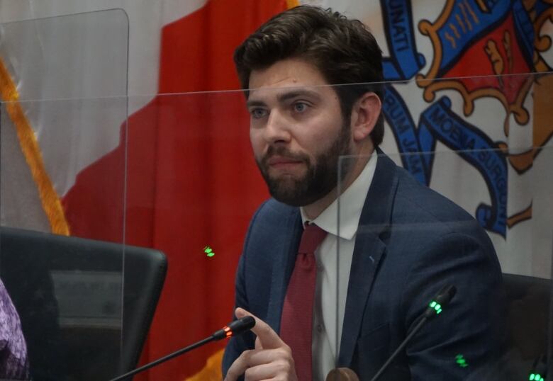 A man in a blue suit, white shirt and red tie looks ahead from his council seat.