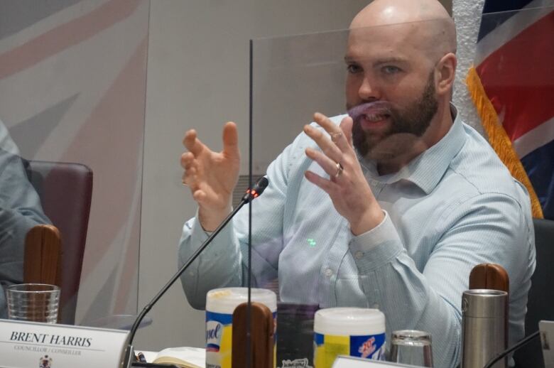 A man holds up his hands as a speaks sitting down. 