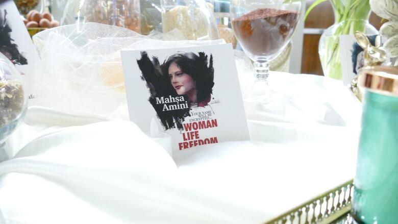 A white card that reads 'Woman Life Freedom' and features the face of Mahsa Amini rests on a table.