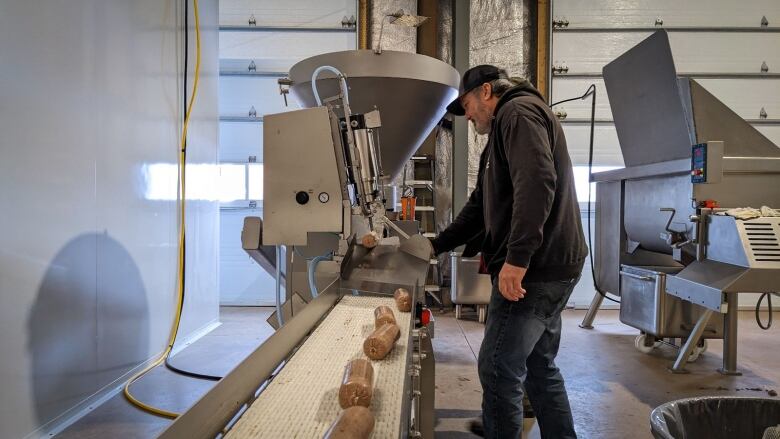 A man stands next to a large machine and a conveyor belt with bait sausages on it.