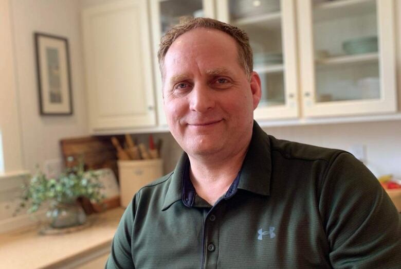 A man poses for a picture in a kitchen wearing a polo.