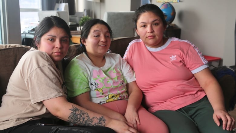 Three young women sit together on a couch. 