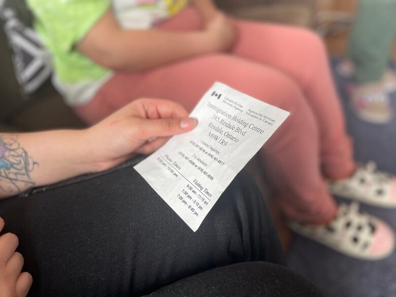 Woman holds piece of paper that has contact information for Immigration Refugee Citizenship Canada.