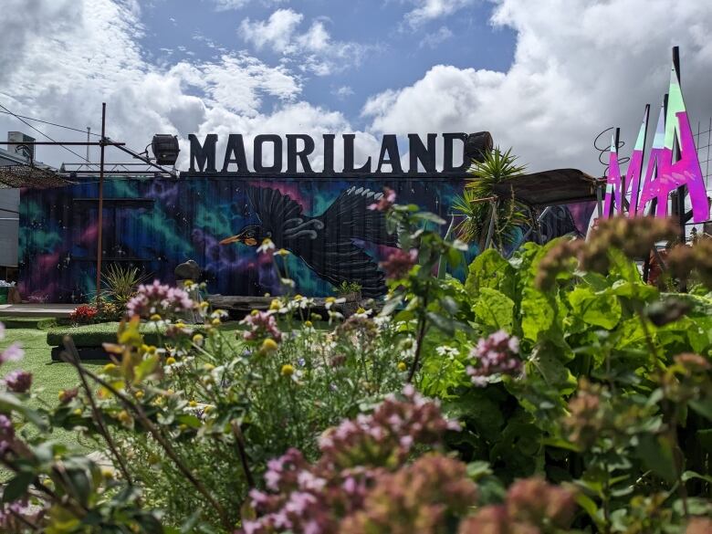 Plants in front of a colorful shipping container painted with a black bird.  