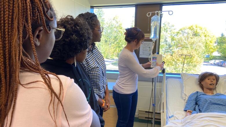 A group of students stand facing a plastic dummy in a hospital bed.