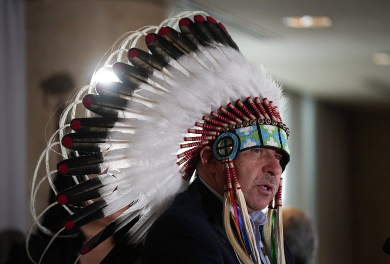 An Indigenous man in a headdress speaks at a news conference.