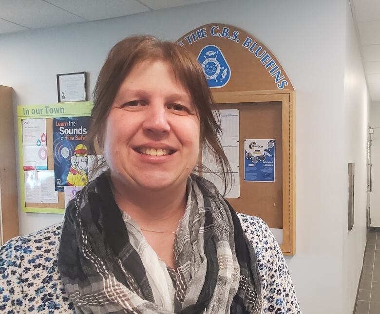 A woman with brown hair stands in the lobby of a recreation center, just outside the squash courts. She's wearing a plaid scarf and a polka dot shirt.