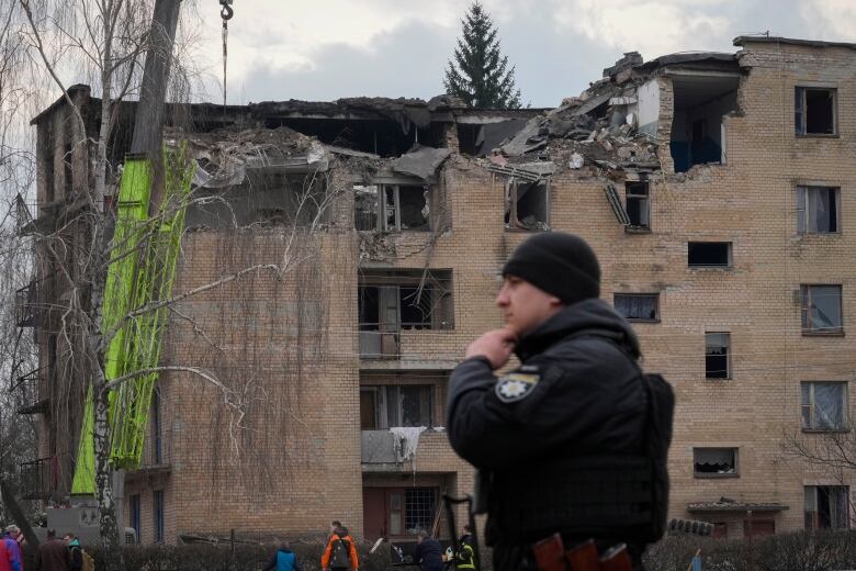 A police officer stands near a missile-damaged building.