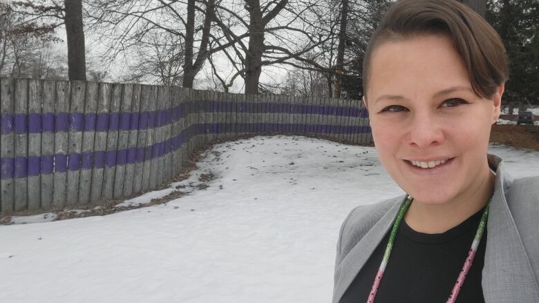 Woman in some snow with a fence behind her. 