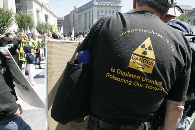 A man, with his back turned, wears a black t-shirt with a yellow radioactive material symbol and the words 