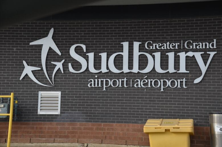 A sign on a brick wall reads 'Greater Sudbury airport'