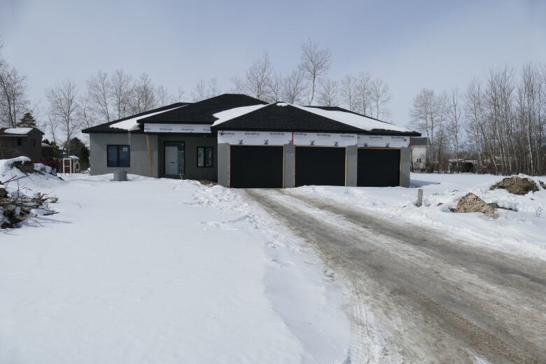 An unfinished home is shown at the end of a long driveway in a rural area.