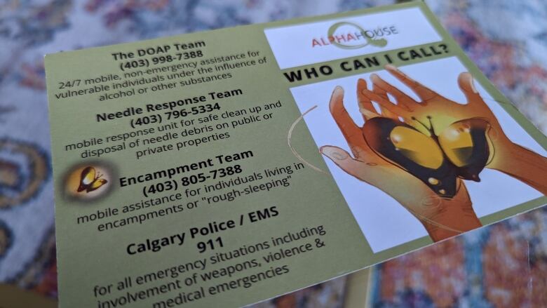 A card on a table is shown with a list of phone numbers to the DOAP team, encampment tea, needle response or 911 and reasons for calling them. 