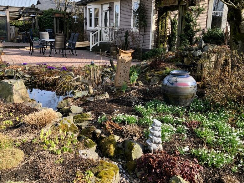 A large ceramic pot and other ceramic objects stand in a garden bed. 