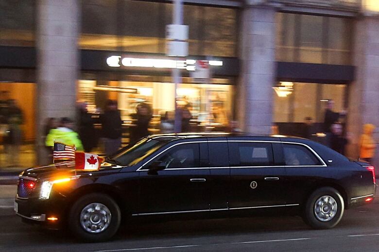 A black car moves past a restaurant in a mall. There's a bit of motion blur.