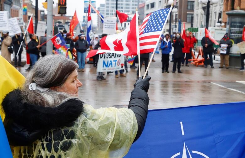 A woman waves a U.S. and Canadian flag across the street from protesters near the U.S. Embassy in Ottawa.