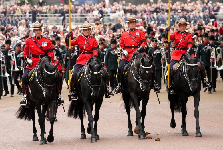 Four Royal Canadian Mounted Police officers ride on horses at the front of a procession.