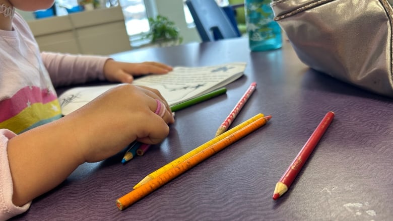 A child's hand clasps a pencil crayon at a desk.