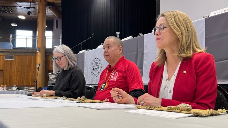 A man is flanked by two women over the long table in a hall.