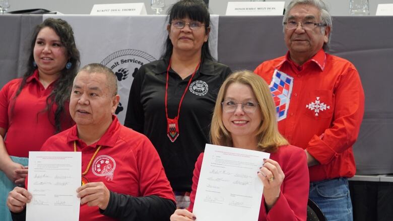 A man and a woman display a document, with people standing behind them.