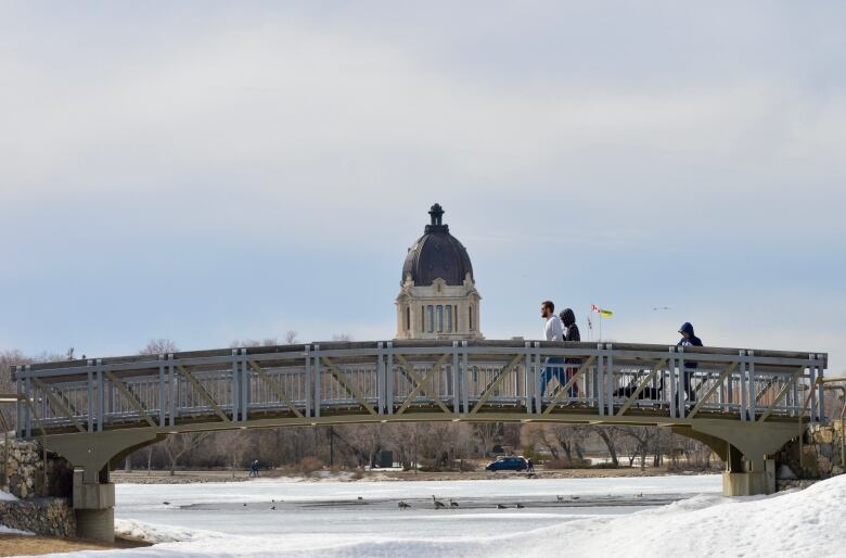 Three people cross a bridge with a domed building in the background