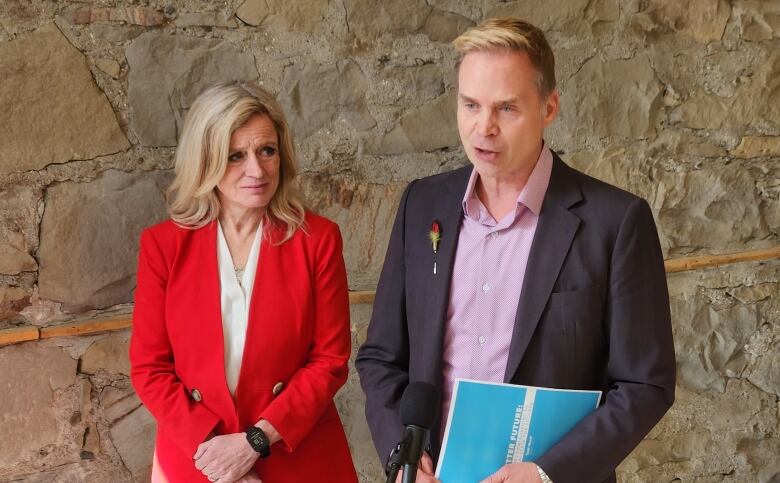 Todd Hirsch, at right, speaks into a microphone while NDP leader Rachel Notley looks on. 