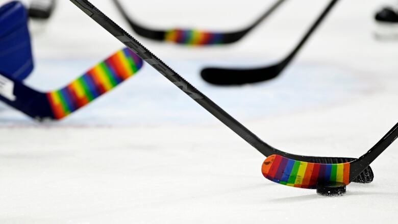 Hockey sticks wrapped in rainbow coloured-tape on the ice. 