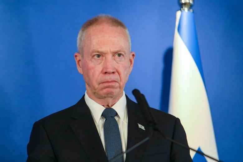 A person delivers a statement to a microphone as the Israel flag is seen in the background.