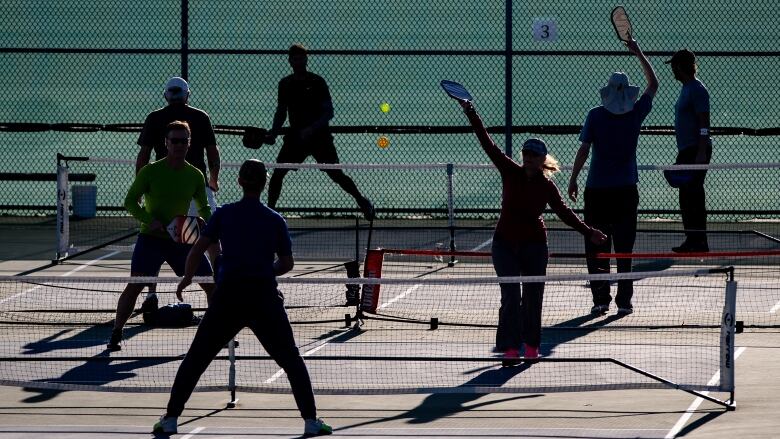 People in silhouette play pickleball.