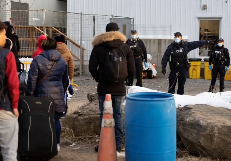 A police officer wearing a mask points to his left as he instructs a small group of migrants on where to go.