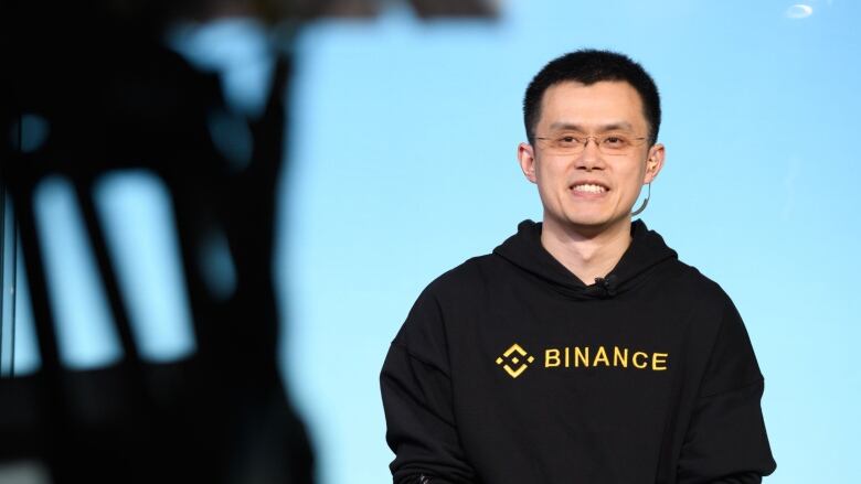 The CEO and founder of crypto trading firm Binance is shown wearing a sweater bearing his company's logo. 