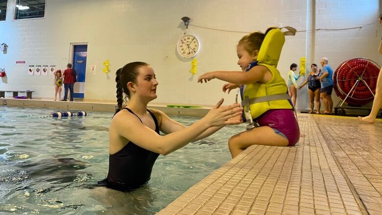 Swim instructor Lalla Mcfarlane helps a young girl get a the pool from the side.