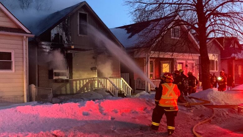 A firefighter sprays water on a smoking house.